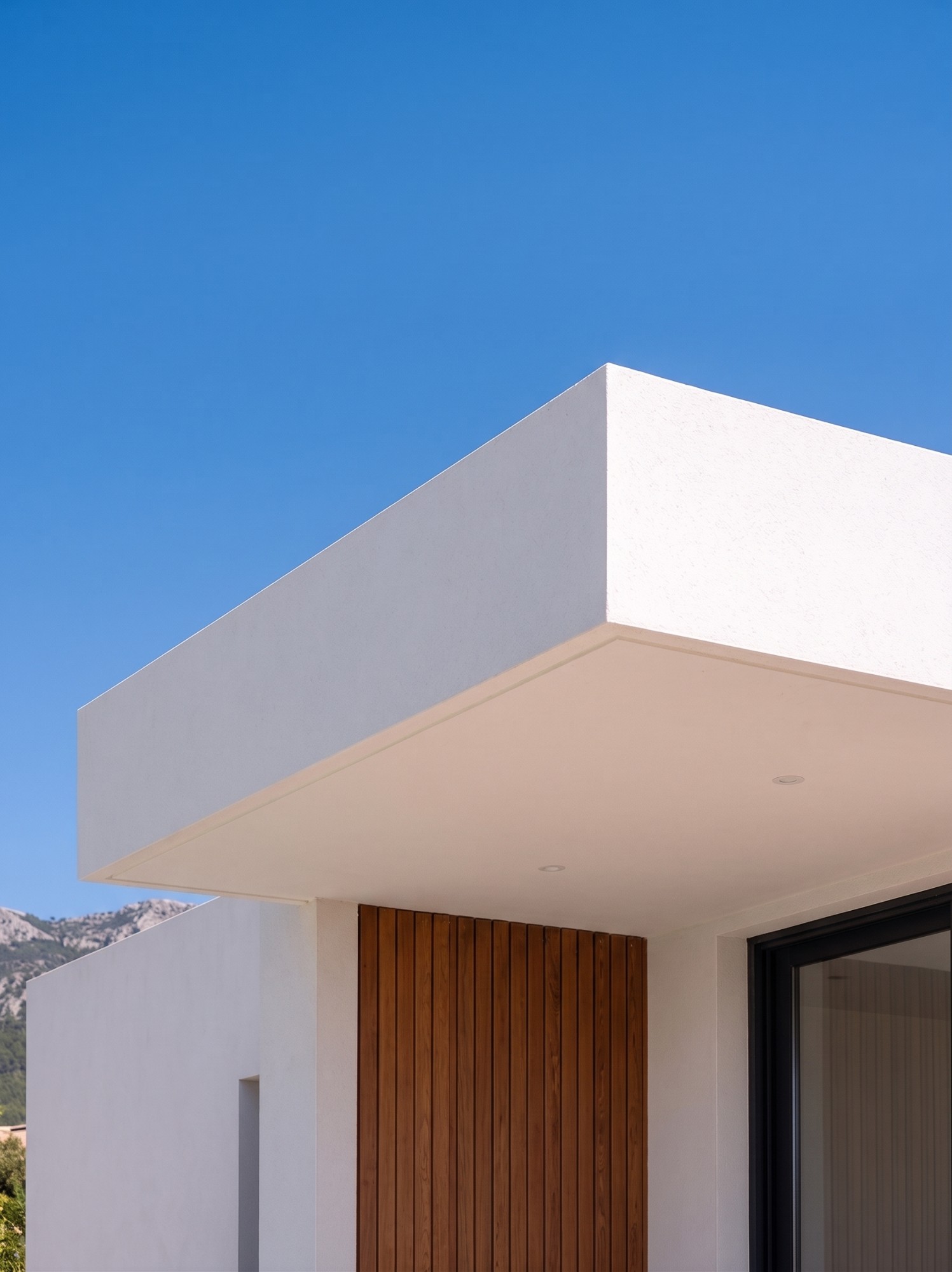 A white cantilevered house roof with timber cladding under a clear blue sky