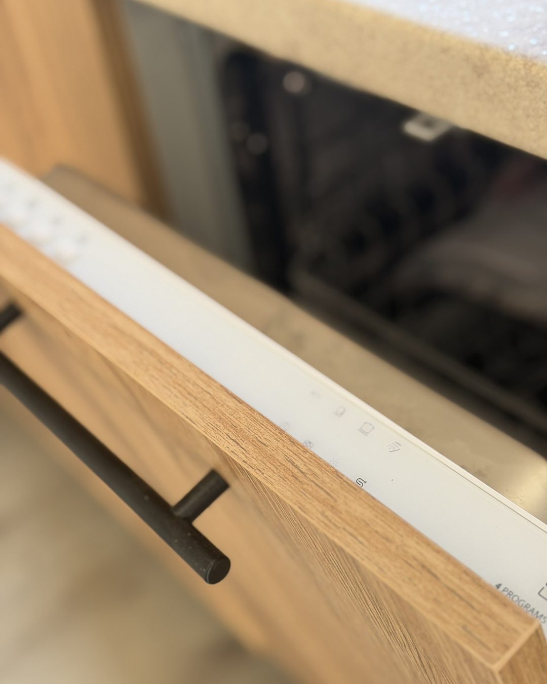 Close-up of an integrated dishwasher behind an oak-effect cabinet panel with a black bar handle in a modern kitchen