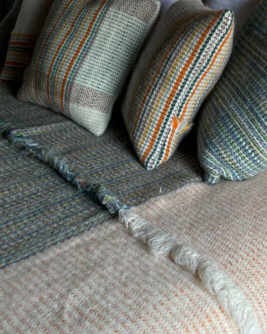 Striped handwoven wool cushions and a fringed throw on a bed in warm, muted tones