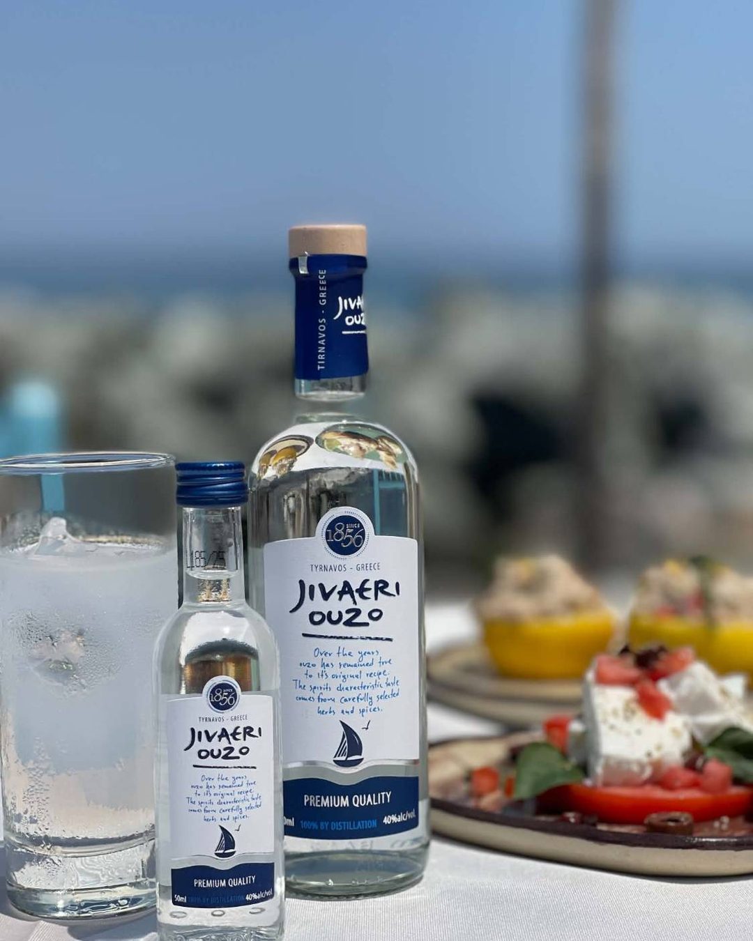 Jivaeri Ouzo bottles from Tyrnavos with an iced glass and Greek meze on a seaside table