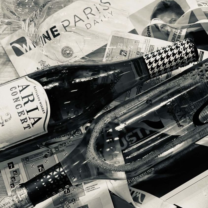 Ασπρόμαυρη νεκρή φύση με αφρώδη οίνο Aria Concert του Οινοποιείου Κατσαρού πάνω σε οδηγούς της Wine Paris, με ποτήρι γευσιγνωσίας